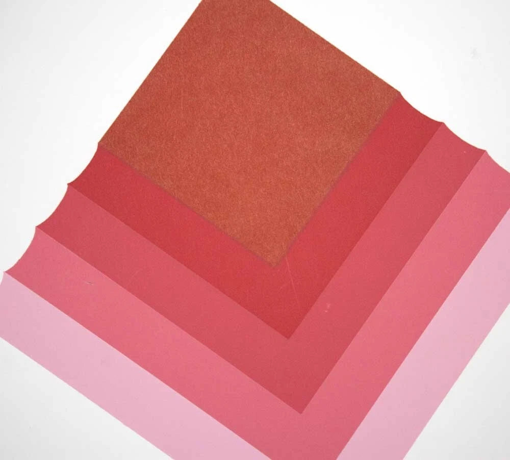 Four square swatches of textured paper in warm pink and red tones, arranged in a nested square pattern on a white background.