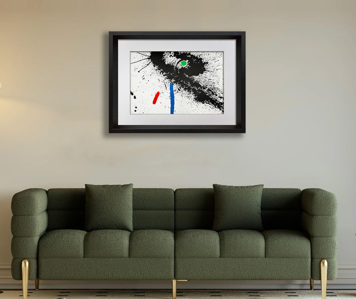 A framed abstract Joan Miro art print featuring black, white, blue, and red paint splatters, displayed on a beige wall above a green sofa.
