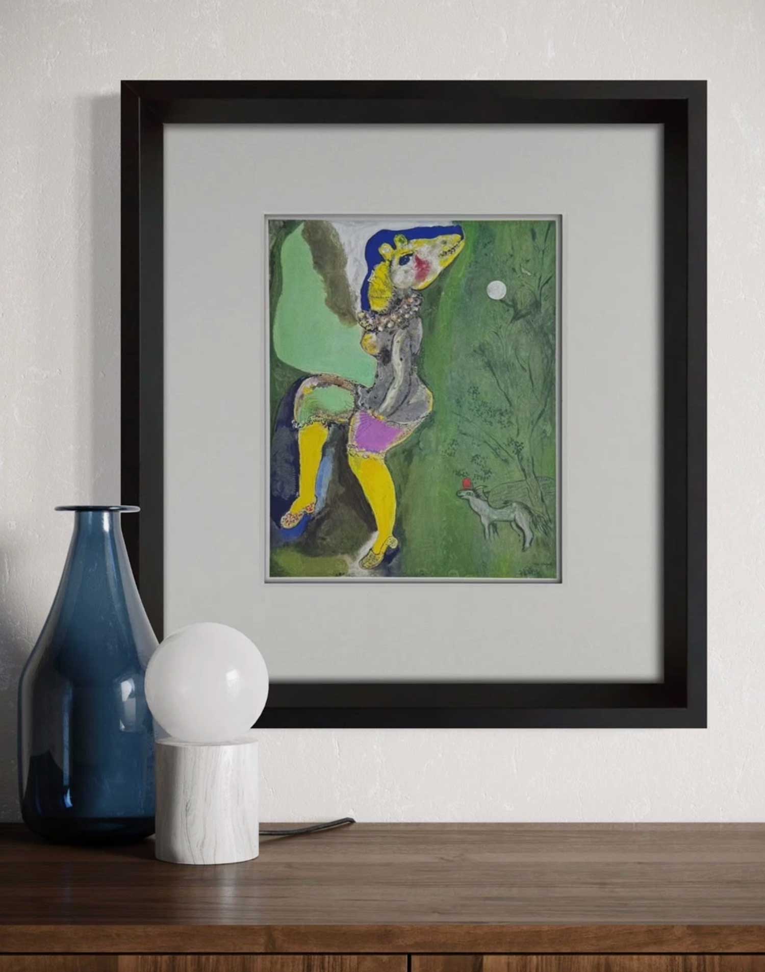 Framed Marc Chagall Lithograph of a colorful character on a wall above a wooden surface with decorative items.