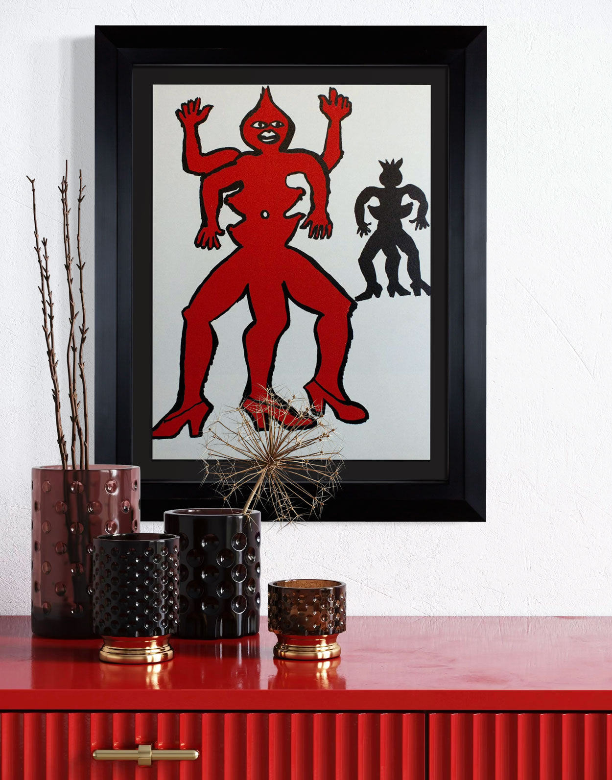 Framed Calder Lithograph of a red and black figure on a white background, displayed on a red surface with decorative items.