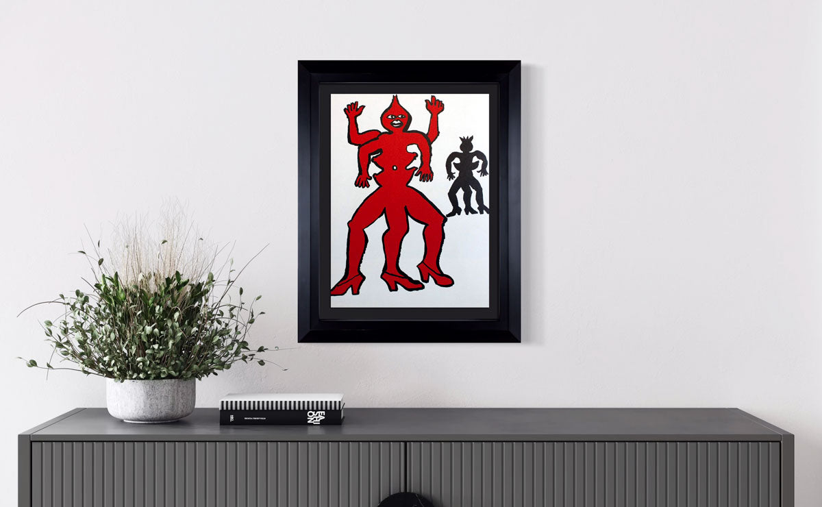 Framed Calder Lithograph of a red and black figure on a white wall above a gray console table.